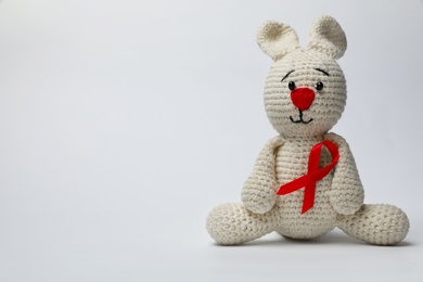 Cute knitted toy bunny with red ribbon on light grey background, space for text. AIDS disease awareness