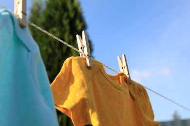Photo of Clean baby onesies hanging on washing line in garden, closeup. Drying clothes
