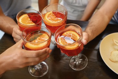 Friends with Aperol spritz cocktails together at wooden table, closeup