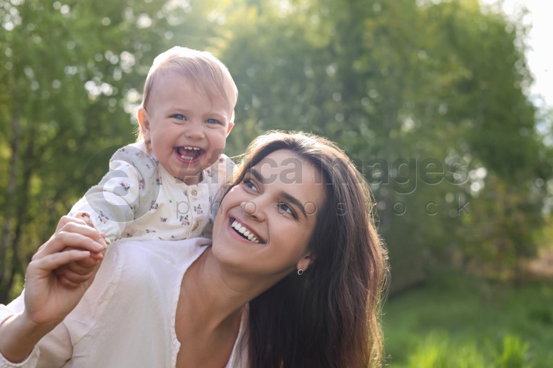 Happy mother playing with her cute baby in park on sunny day. Space for text