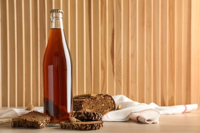 Photo of Bottle of delicious fresh kvass, spikelets and bread on wooden table. Space for text