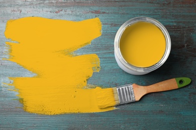 Can of yellow paint and brush on teal wooden background, flat lay. Space for text