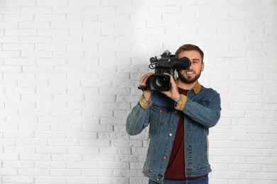Operator with professional video camera near white brick wall, space for text