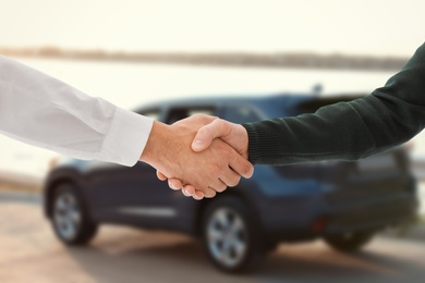 Man buying car and shaking hands with salesman against blurred auto, closeup