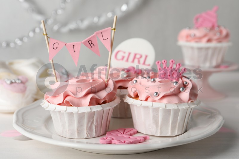 Photo of Delicious cupcakes with pink cream and toppers for baby shower on white wooden table
