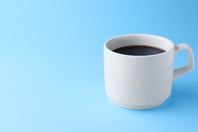 White mug of freshly brewed hot coffee on light blue background, space for text
