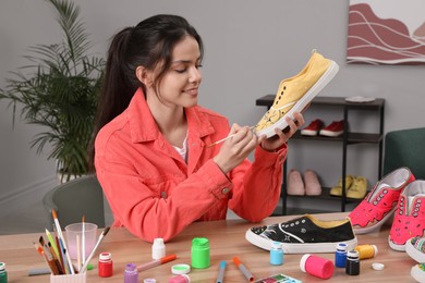 Woman painting on sneaker at wooden table indoors. Customized shoes