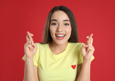Excited young woman holding fingers crossed on red background. Superstition for good luck