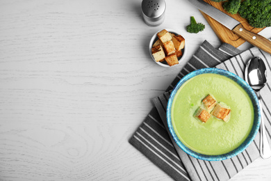 Delicious broccoli cream soup with croutons served on wooden table, flat lay. Space for text