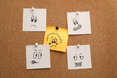 Yellow paper note with drawn sad face among aggressive ones pinned to cork board. Racism concept
