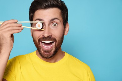 Photo of Funny man hiding his eye with tasty sushi roll on light blue background, closeup. Space for text
