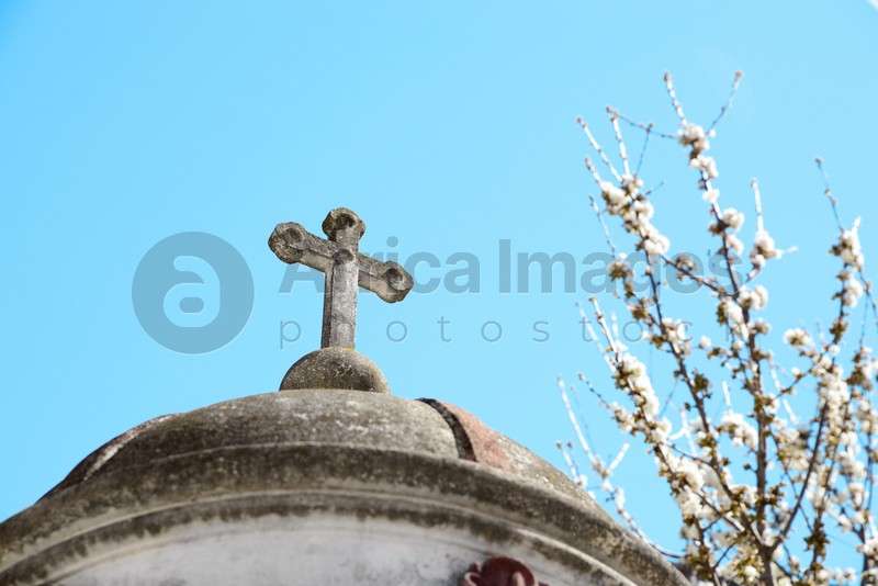 Roof of old chapel with stone cross near blossoming tree against blue sky, closeup
