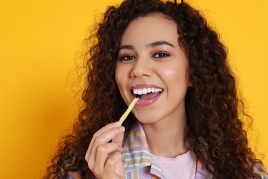 African American woman eating French fries on yellow background