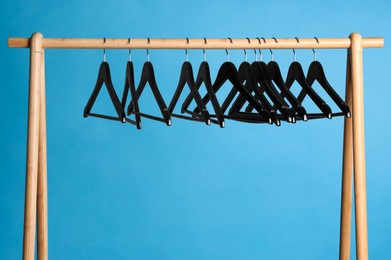 Photo of Black clothes hangers on wooden rack against light blue background