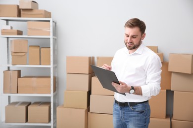 Young businessman with clipboard near cardboard boxes at warehouse