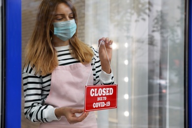 Business owner in mask hanging red sign with text Closed Due To Covid-19 onto glass door. Coronavirus quarantine