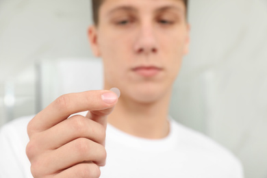 Teen guy using acne healing patch indoors, focus on hand