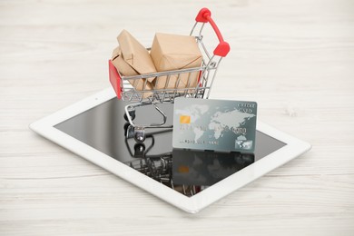 Photo of Online payment concept. Small shopping cart with bank card, boxes and tablet on white table