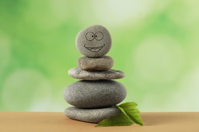 Stack of stones with drawn happy face and green leaves on table against blurred background. Zen concept