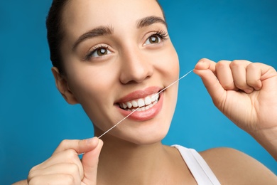 Young woman flossing her teeth on blue background. Cosmetic dentistry