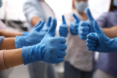 Group of people in blue medical gloves showing thumbs up on blurred background, closeup