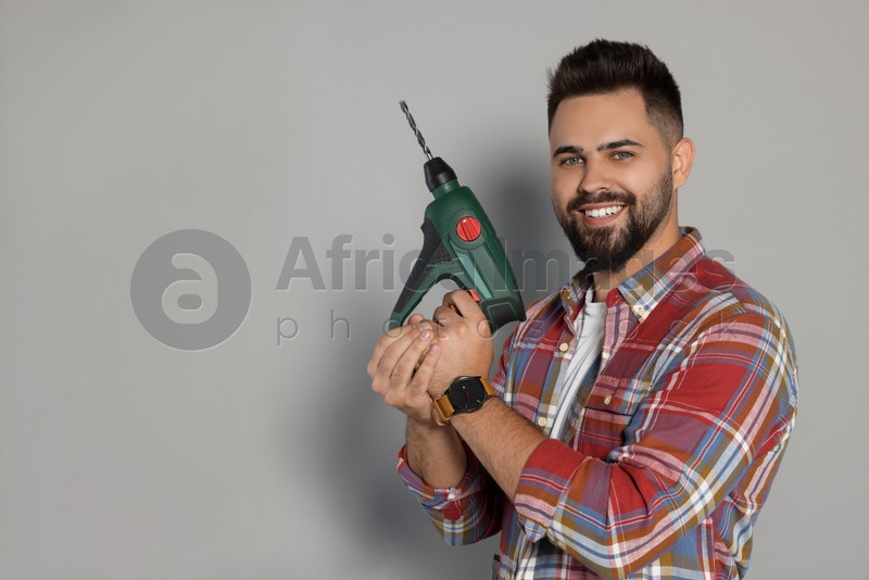 Young man with power drill on grey background. Space for text