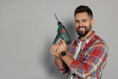 Young man with power drill on grey background. Space for text