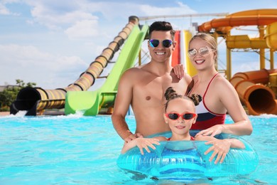 Happy family with inflatable ring in swimming pool at water park, space for text