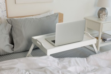 White tray table with laptop on bed indoors