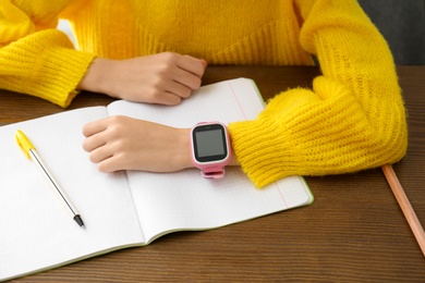 Girl with stylish smart watch at wooden table in school, closeup