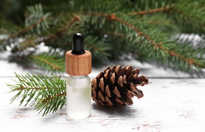 Bottle of pine essential oil, conifer tree branches and cone on white wooden table