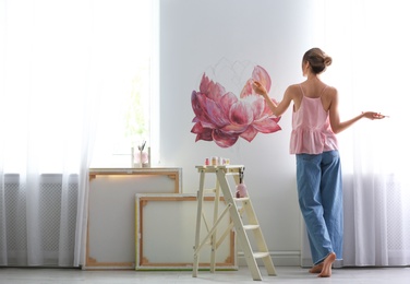 Decorator painting flower on white wall in room. Interior design