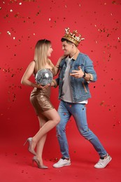 Happy couple with disco ball and confetti on red background