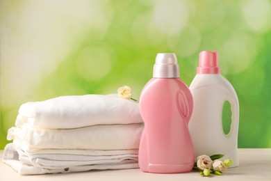 Photo of Bottles of laundry detergents, clean clothes and roses on white wooden table