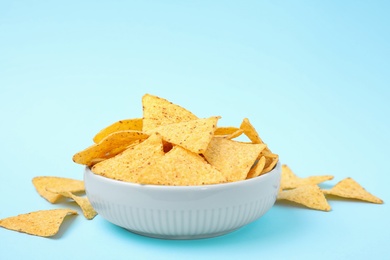 Bowl with tasty Mexican nachos chips on light blue background, space for text