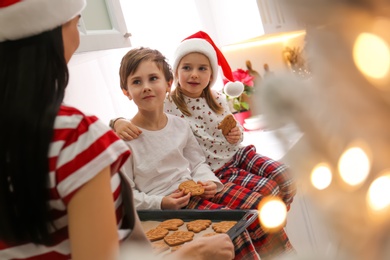 Mother giving her cute little children freshly baked Christmas cookies in kitchen
