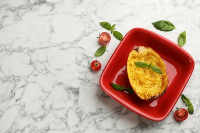 Photo of Half of cooked spaghetti squash in baking dish, tomatoes and basil on white marble table, flat lay. Space for text