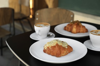 Tasty croissants and cups of aromatic coffee on black table in cafeteria