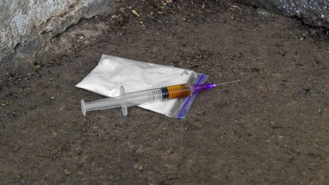 Photo of Plastic bag with powder and syringe on asphalt outdoors. Hard drugs