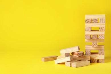Jenga tower and wooden blocks on yellow background, space for text