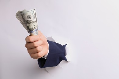 Businessman breaking through white paper with money in fist, closeup. Space for text