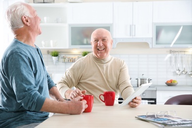 Elderly men using tablet PC at table in kitchen