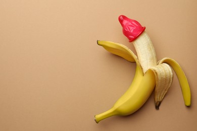 Banana with condom on pale orange background, top view and space for text. Safe sex concept