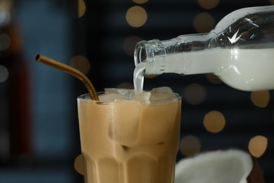 Photo of Pouring syrup into glass of tasty iced coffee against blurred lights, closeup
