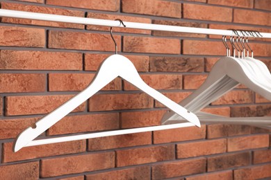 White clothes hangers on rail near red brick wall