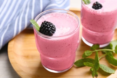 Delicious blackberry smoothie in glasses on wooden tray, closeup