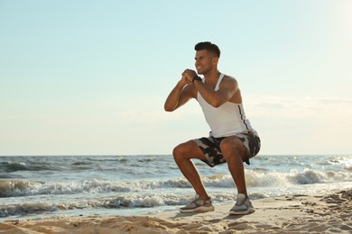 Sporty man doing exercise on sandy beach at sunset