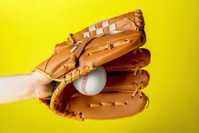 Photo of Baseball player holding ball with catcher's mitt on yellow background, closeup. Sports game