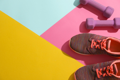Dumbbells, sneakers and space for text on color background, flat lay. Physical fitness