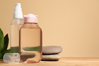 Photo of Bottles of micellar water, green leaves and spa stones on wooden table against beige background. Space for text